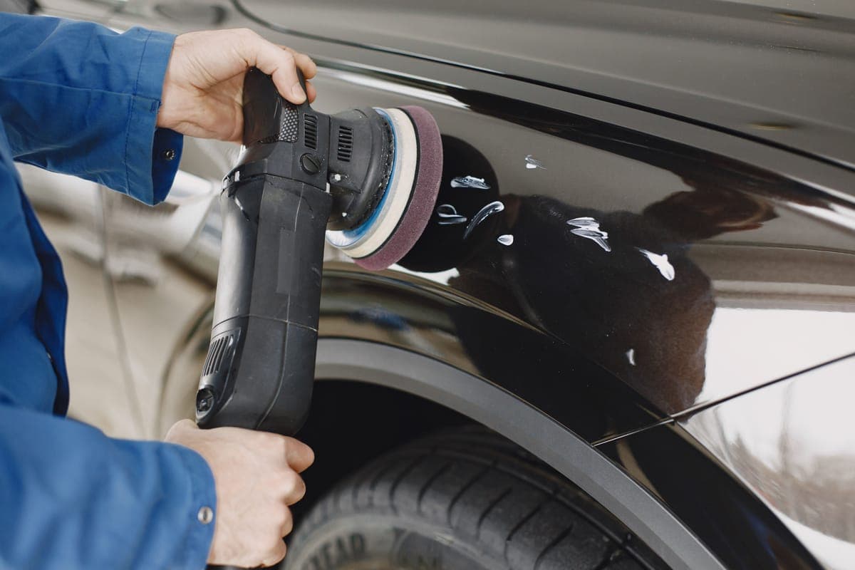 A dual action polisher with a cream foam pad resting on a bright car panel