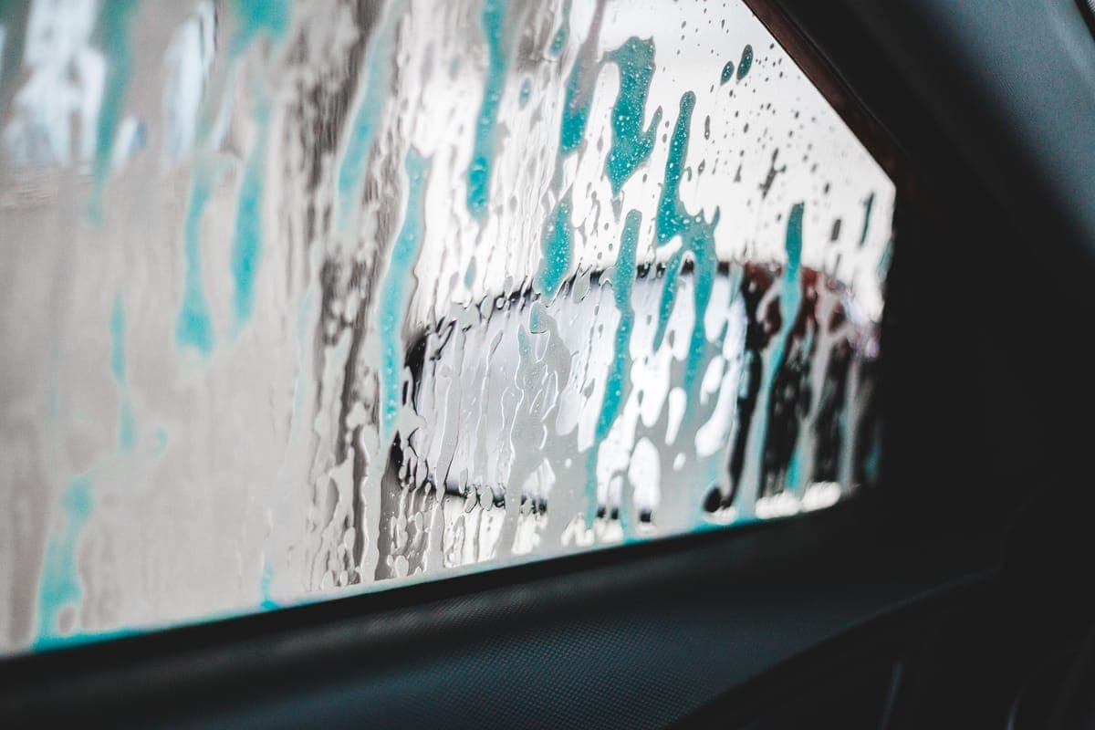 A wash mitt lifting suds from a bucket beside a clean car in daylight