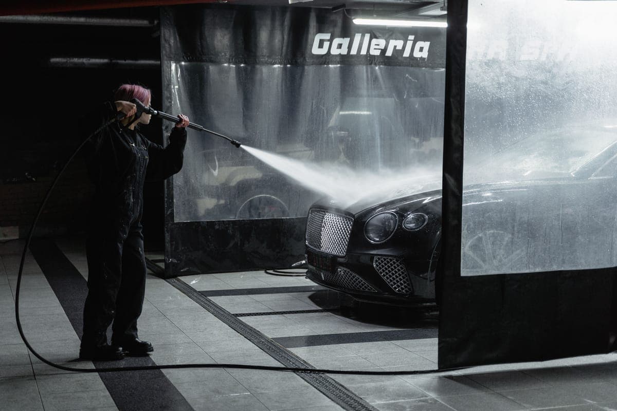 An electric pressure washer and coiled hose beside a clean car on a bright driveway