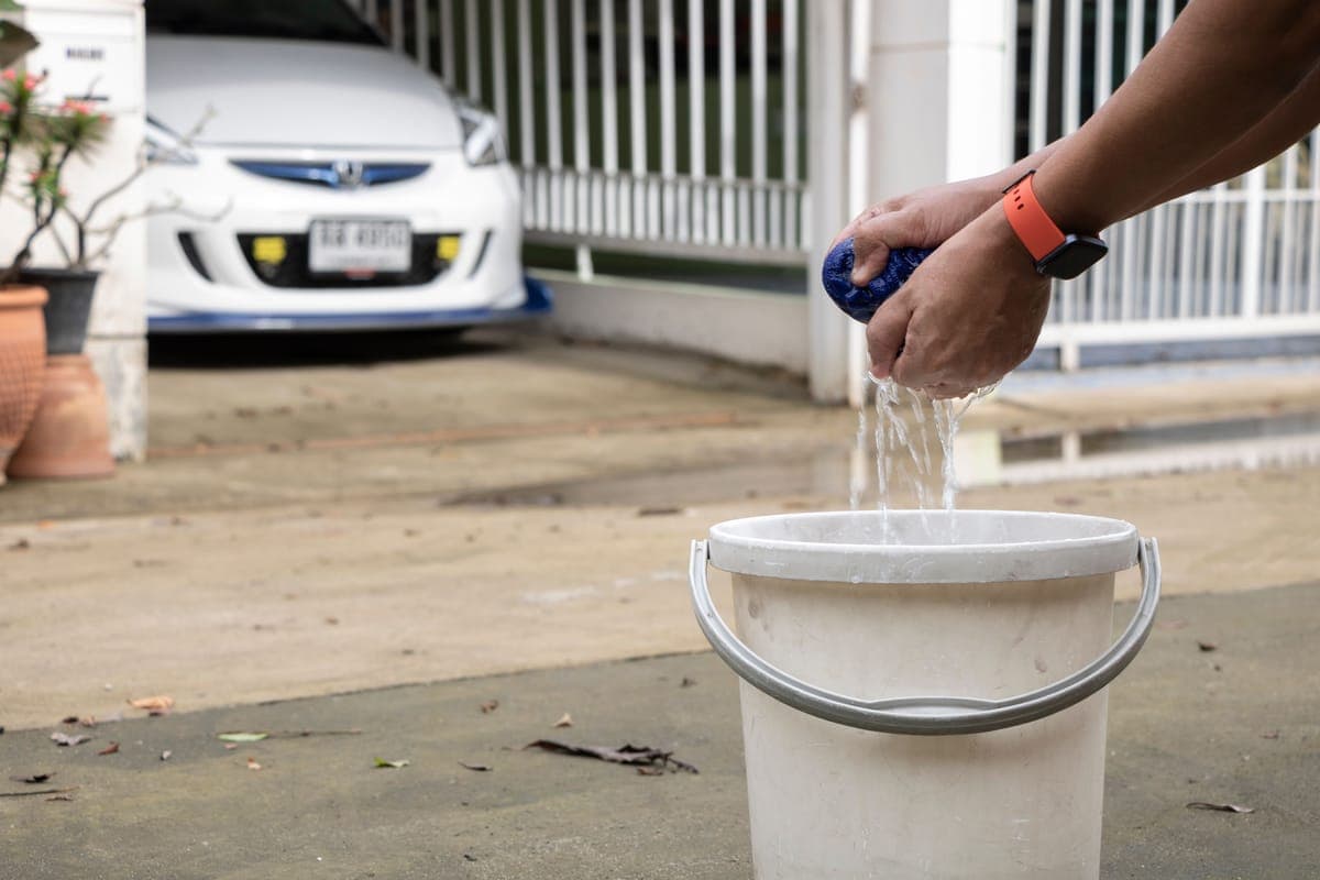 A bucket of rinseless solution and folded towels beside a car in a parking area