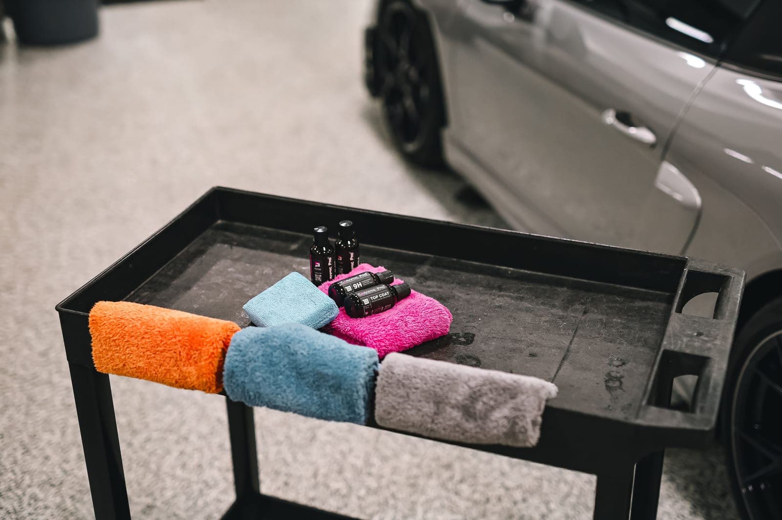 A stack of folded microfiber towels beside detailing brushes on a bright workbench